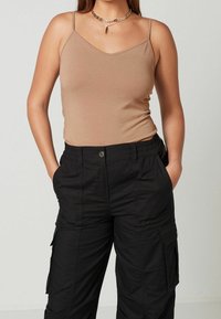 Top senza maniche color tan con scollatura a V, abbinato a pantaloni cargo neri con tasche e vita elastica. Tessuto dalla texture liscia.