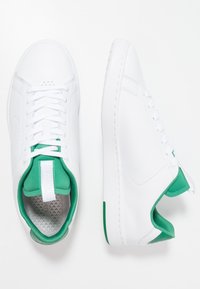 Paire de baskets basses blanches avec doublure intérieure verte, lacets blancs et semelle intérieure grise texturée, vues de dessus et de côté.