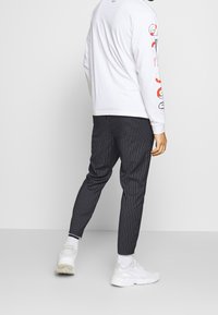 Svartvita randiga byxor, slim fit med en slät yta. Kombineras med en långärmad vit skjorta och vita sneakers.