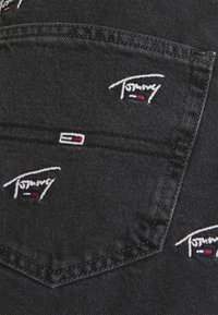 Tela de mezclilla negra con múltiples logotipos bordados. Los logotipos son blancos con detalles en rojo y azul, ubicados en los bolsillos. Costuras limpias.