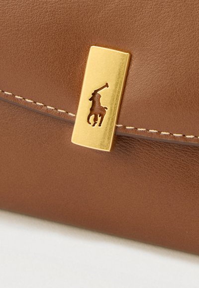 Ruskea nahkapinta, jossa on kullanvärinen suorakulmainen lukko, jossa on leikattu hevosen selässä ratsastavan polopelaajan siluetti.