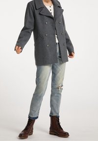 Grå dobbeltradet uldfrakke med store revers, sidelommer, parret med lyseblå slidte jeans og brune snørebåndsstøvler.