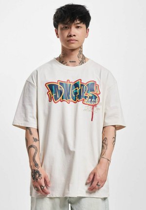 Camiseta de algodón crema de gran tamaño con un gráfico multicolor estilo graffiti en el frente, con mangas cortas y un ajuste relajado.