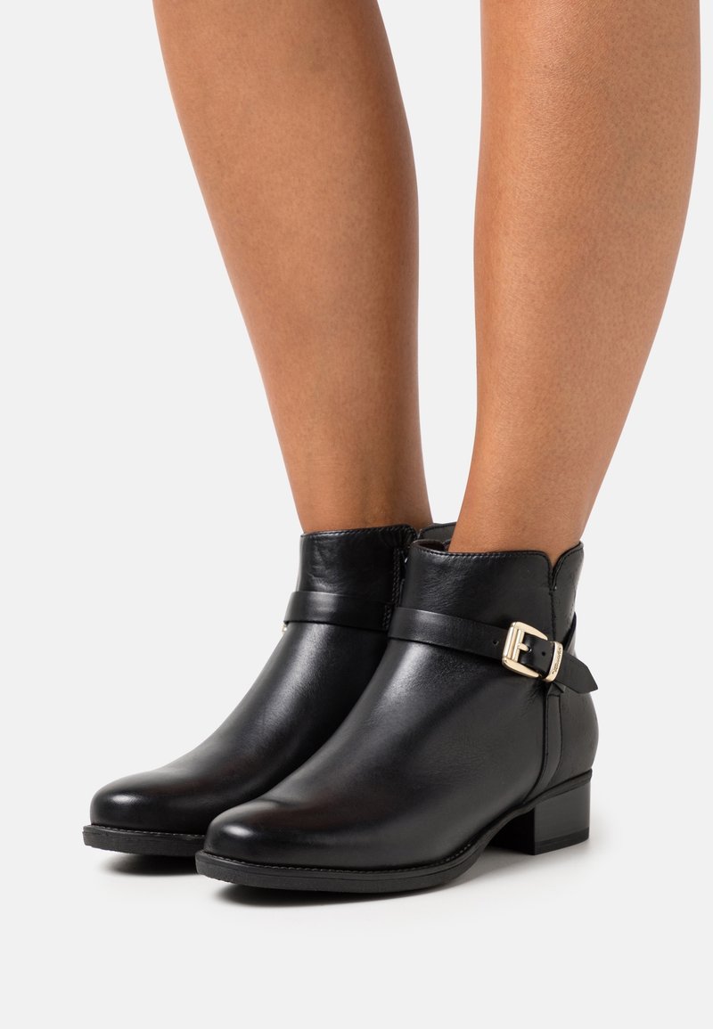 Botines de cuero negro con punta redonda, tacón bajo en bloque y una correa con un detalle de hebilla metálica. Textura suave en toda su superficie.