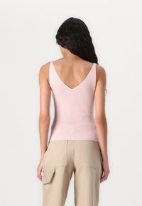 Różowy, prążkowany top na ramiączkach z tyłu w kroku V. Materiał wydaje się miękki i dopasowany, uzupełniony cienkimi ramiączkami.