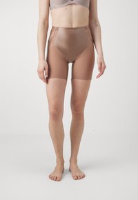 Pantalones cortos moldeadores de cintura alta en marrón claro, con un material suave, elástico y semitranslúcido, diseño ajustado y longitud a mitad del muslo.