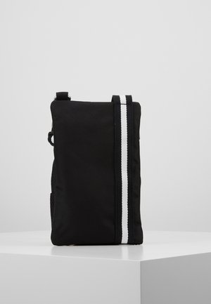Black rectangular crossbody bag with one vertical white stripe, standing upright on a white pedestal against a plain background.