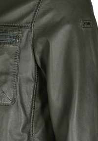 Dunkelgrüne Lederjacke mit einer zippten Brusttasche, strukturiertem Finish und detaillierter Naht an der Schulternaht.