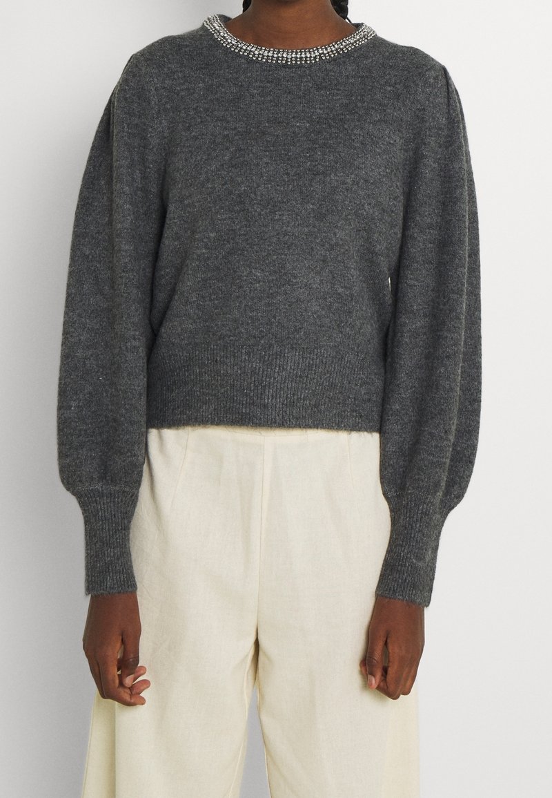 Pull en maille gris foncé avec manches longues bouffantes et encolure perlée, porté avec un pantalon large taille haute écru.