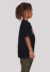 Black t-shirt with short sleeves and a crew neck, featuring red and white graphic text. Worn with olive green cargo pants.