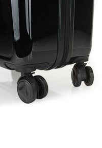 Maleta rígida negra con una superficie lisa y brillante, que cuenta con dos ruedas negras y un cierre con cremallera en uno de los lados.