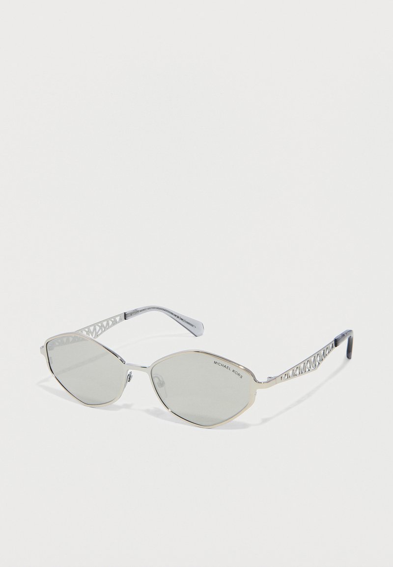 Γυαλιά ηλίου Michael Kors με ασημένια σκελετό, γκρι φακούς σε γωνιώδη σχήματα και μπράτσα με σχέδιο πλέγματος, σε λευκό φόντο.