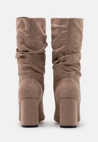 Tan suede knee-high boots with a slouch design, block heels, and a smooth texture. Features rounded tops and subtle stitching details.