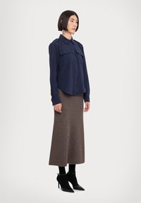 Navy blue button-up shirt with two chest pockets, paired with a brown ribbed maxi skirt and black ankle boots with pointed toes.