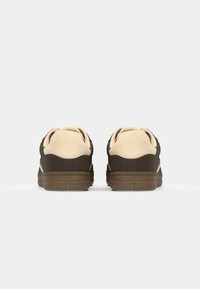 Braune und cremefarbene Sportschuhe mit einer glatten oberen Oberfläche, runder Zehenpartie, gepolstertem Kragen und profiliertem Gummisohle, entworfen für Komfort und Unterstützung.