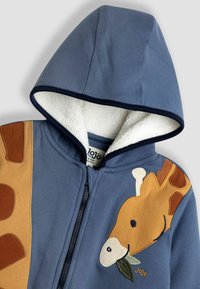 Hanorac cu fermoar pentru copii, de culoare albastră, căptușit cu fleece alb, având un aplicație cu o girafă care ține o frunză în bot pe față.