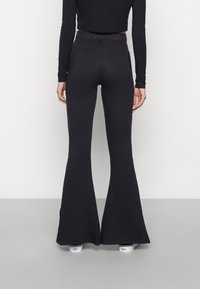 Svarta utsvängda byxor i ett mjukt, stretchigt tyg, med hög midja och en slät yta. Inga synliga mönster eller dekorationer.