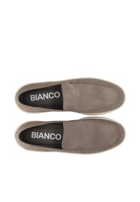 Tan ruskinds slip-on sko med en glat tekstur, der har en rund tå, elastiske sideaccenter og en lys farvet sål. Brandlogoet er synligt.