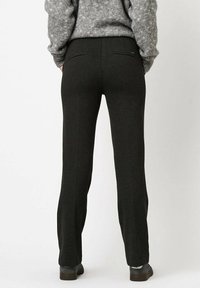 Pantalons noirs en tissu doux et texturé, avec une coupe droite, des poches arrière et un accent minimaliste de la marque sur la ceinture.