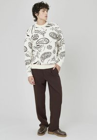 Pull en crème tricoté avec un motif paisley marron, col et poignets côtelés, associé à un pantalon marron et des chaussures marron avec une semelle texturée.