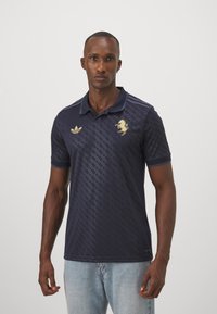 Marineblaues Poloshirt mit strukturiertem Muster, goldenem Löwenemblem und Dreistreifenakzenten auf den Schultern. Aus atmungsaktivem Material gefertigt.