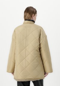 Beige prošívaná bunda s vysokým límcem, se měkkou texturou a fleecovým podšívkou na spodním lemu. Exteriér s diamantovým vzorem.