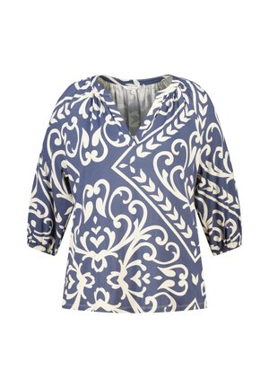 Blouse bleue avec un motif floral et géométrique blanc complexe, manches trois-quarts bouffantes et décolleté en V avec encolure froncée.