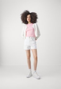 Pantalones cortos de mezclilla blanca con dobladillo deshilachado, camiseta ajustada rosa y cárdigan blanco. Las zapatillas blancas de plataforma completan el conjunto.