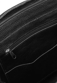 Interno di una borsa in pelle nera con finitura testurizzata, due cerniere e una fodera liscia. Presenta cuciture distintive lungo i bordi.