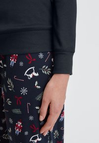Donker sweatshirt met geribbelde manchetten, gecombineerd met gevlekte pyjamabroek met feestelijke motieven zoals notenkrakers, hulst en sneeuwvlokken.
