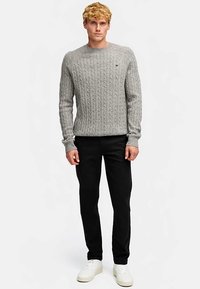 Grå stickad tröja med texturerad kabeldesign, rund halsringning och långa ärmar, kombinerad med svarta byxor och vita sneakers.