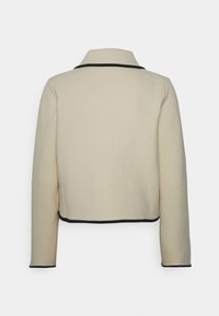 Veste courte couleur crème avec une finition texturée, dotée d'une bordure noire le long du col et de l'ourlet inférieur, avec des manches longues.