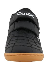 Baskets noires avec un dessus en synthétique texturé, deux bandes Velcro, et une semelle en caoutchouc beige. Présente des coutures et un logo sur le côté.