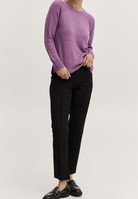 Lila gestrickter Pullover mit geripptem Rundhalskragen und seitlichen Schlitzen, kombiniert mit schwarzen maßgeschneiderten Hosen und schwarzen Loafers. Schlichtes, modernes Design.