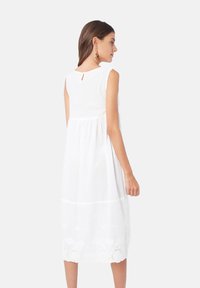 Vestido sin mangas blanco con un escote en forma de llave en la espalda, con un diseño en capas y un borde de encaje en el dobladillo, hecho de una tela ligera.