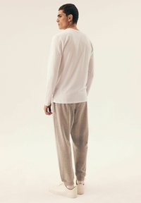 Langarm weißes Hemd kombiniert mit grauen Sweatpants; glattes Material, entspannte Passform und weiße Sneaker vervollständigen das lässige Outfit.