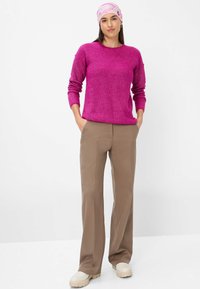 Fuchsiastrickpullover mit Rundhalsausschnitt, lockerer Passform und langen Ärmeln, kombiniert mit beigen weit geschnittenen Hosen und cremefarbenen Plateauschuhen.