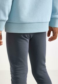 Light blue sweatshirt with ribbed hem and cuffs, paired with fitted dark gray leggings. Smooth texture and casual design.