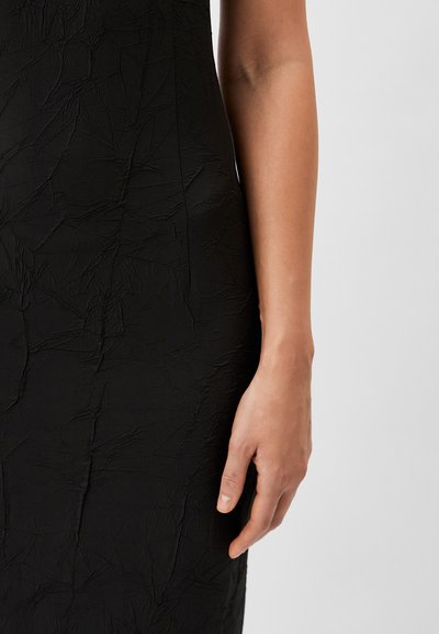 Black dress featuring crinkled texture. Close-up of a hand resting against the dress, highlighting the figure-hugging design.