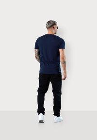 Navy blue short-sleeve t-shirt made from cotton, paired with black pants and white sneakers. Features tattoo details on arms.