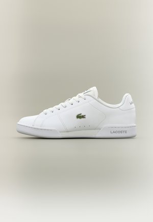 Biały niski sneaker Lacoste z zielonym logo krokodyla oraz napisem "Lacoste" wytłoczonym na podeszwie i pięcie na neutralnym tle.