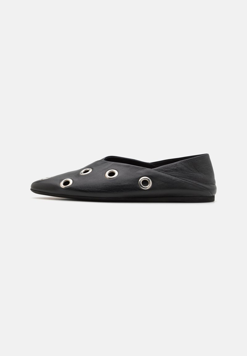 Chaussure plate noire à bout pointu avec cinq grands œillets argentés sur le côté, présentée sur un fond blanc uni.