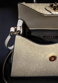 Bolso de mano dorado con acabado suave y texturizado, que presenta un cierre de botón a presión dorado, correa ajustable y un compartimento interior con cremallera.