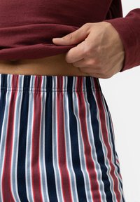 Gestreepte pyjamabroek met een marineblauwe basis, voorzien van verticale strepen in rood, wit en lichtblauw. Elastische tailleband zichtbaar. Zachte stoftextuur.