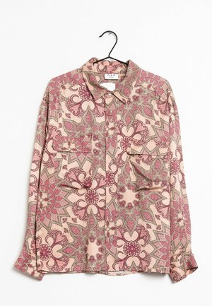 Chemise à manches longues boutonnée avec motif floral paisley rose et beige suspendue sur un cintre noir sur fond blanc.