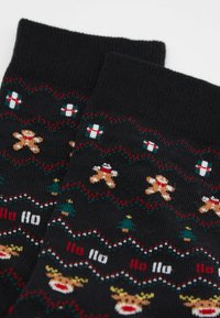 Černé vánoční ponožky s vzory perníčků, dárkových krabic, zelených stromků, nápisem „Ho Ho“ a tvářemi sobů v červené, bílé a zelené barvě.