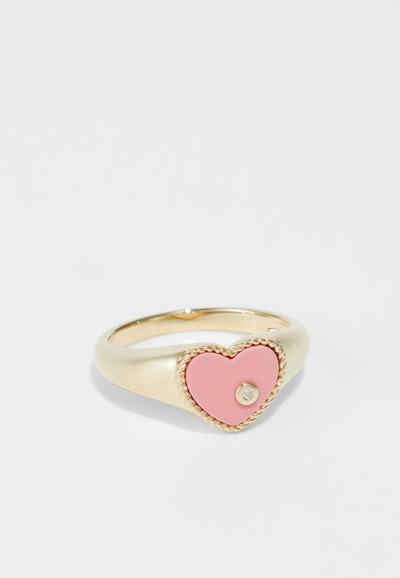 Anillo en tono dorado con un centro en forma de corazón rosa y un pequeño acento de diamante, con un detalle texturizado de cuerda alrededor de la forma del corazón.