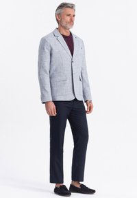 Helle graue strukturierte Blazer mit Revers, einzelner Knopfverschluss, kombiniert mit einem kastanienbraunen Hemd, navyblauen Stoffhosen und schwarzen Slippern.