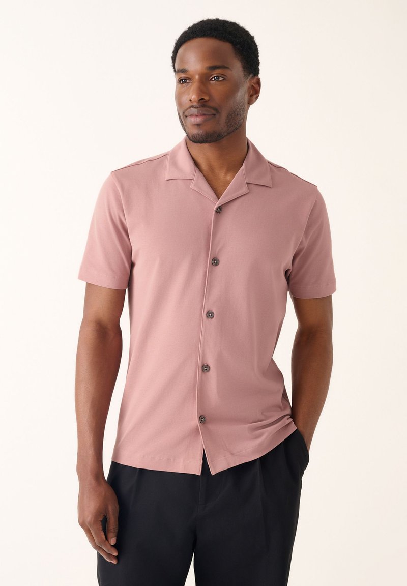 Camicia a manica corta in tessuto rosa tenue, con colletto e chiusura frontale con bottoni scuri, caratterizzata da una vestibilità comoda.