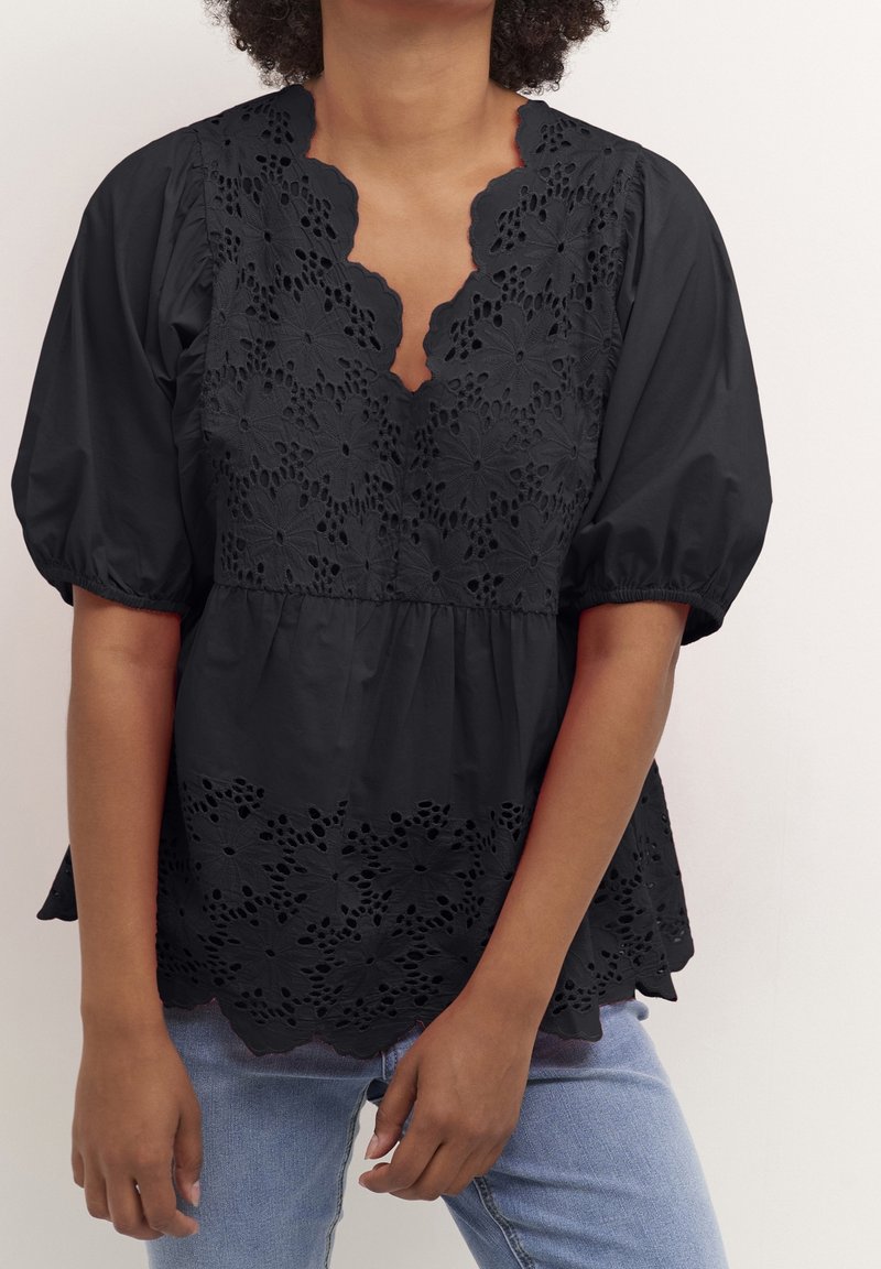 Musta pusero, jossa on puffihihoja, uurrettu helma ja monimutkainen leikattu kukkakuosi kaula-aukossa ja alareunassa.